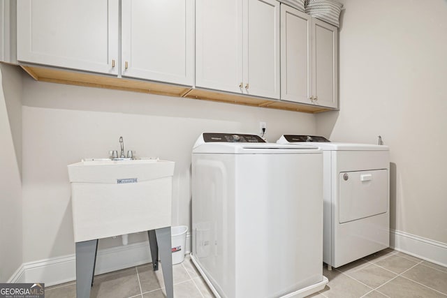 clothes washing area with a sink, cabinet space, light tile patterned flooring, baseboards, and washing machine and clothes dryer