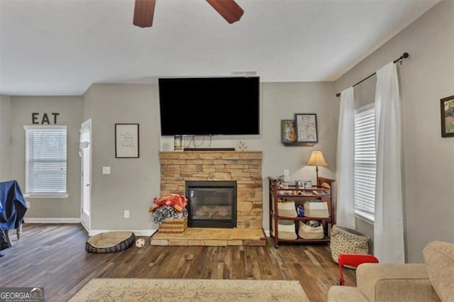 living area featuring baseboards, a ceiling fan, wood finished floors, and a fireplace