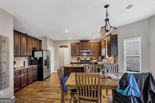 kitchen with wood finished floors, visible vents, decorative backsplash, appliances with stainless steel finishes, and pendant lighting