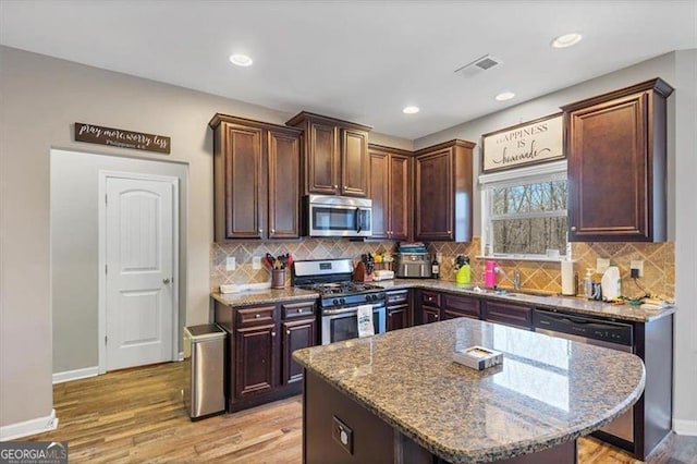 kitchen with light wood finished floors, visible vents, stone counters, stainless steel appliances, and a sink