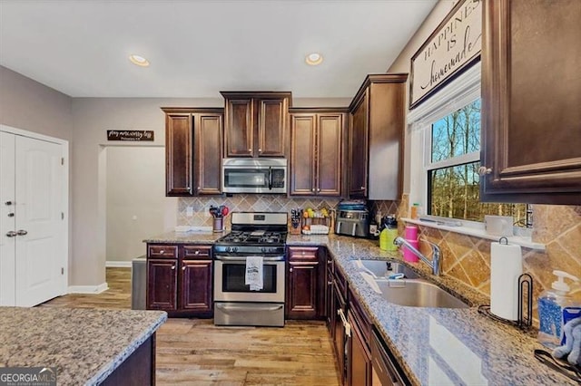 kitchen with backsplash, light stone countertops, light wood-type flooring, appliances with stainless steel finishes, and a sink