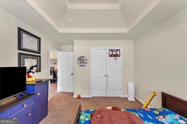 bedroom featuring a tray ceiling, carpet, baseboards, and a closet