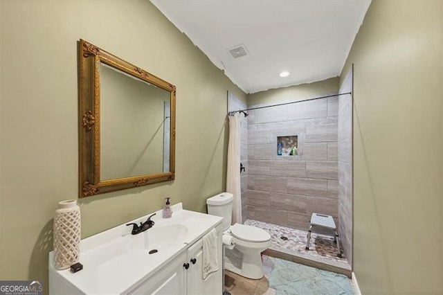 bathroom featuring visible vents, toilet, vanity, and a tile shower