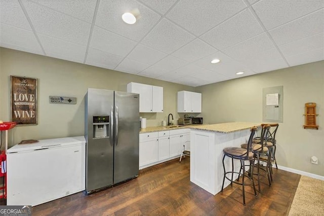 kitchen featuring a kitchen breakfast bar, stainless steel fridge, refrigerator, white cabinetry, and a sink