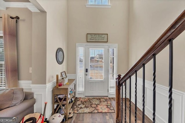 foyer entrance featuring stairway, a decorative wall, wood finished floors, and wainscoting