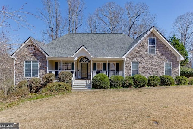 ranch-style home featuring stone siding, roof with shingles, covered porch, and a front lawn