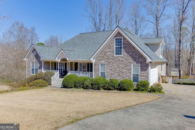 view of front of house featuring stone siding, an attached garage, covered porch, and driveway