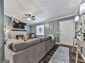 living room featuring wood finished floors, crown molding, baseboards, a brick fireplace, and ceiling fan