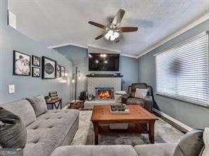 living area with a ceiling fan, a lit fireplace, and ornamental molding