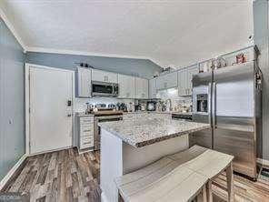 kitchen with appliances with stainless steel finishes, a kitchen island, lofted ceiling, and wood finished floors