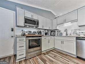 kitchen featuring dark wood finished floors, vaulted ceiling, appliances with stainless steel finishes, white cabinets, and a sink