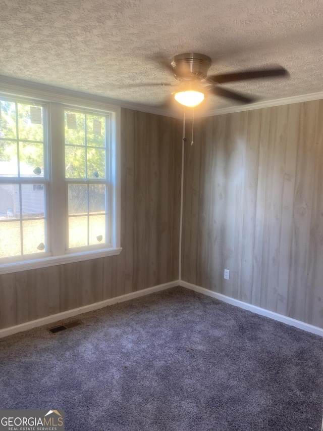 carpeted spare room with plenty of natural light, visible vents, wood walls, and a textured ceiling