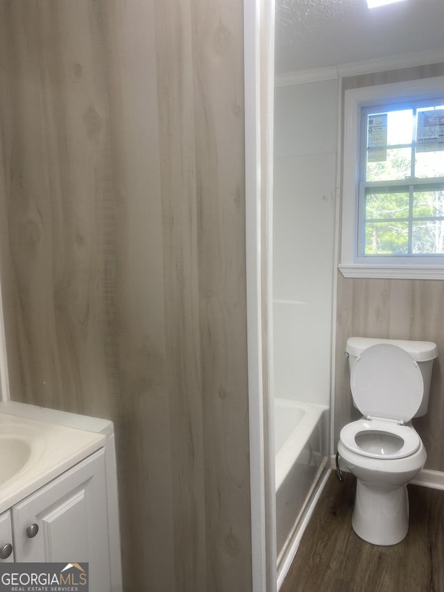 bathroom featuring toilet, vanity, a tub to relax in, wood finished floors, and a textured ceiling