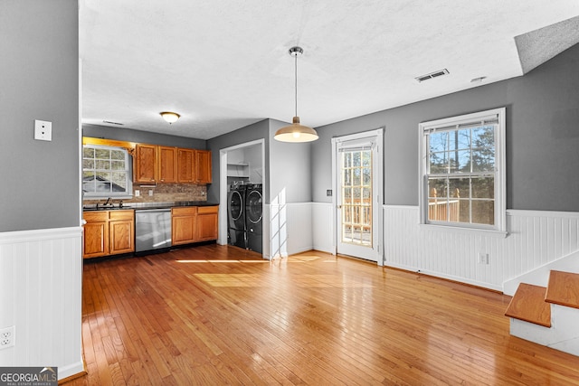 kitchen with visible vents, washer and clothes dryer, wainscoting, brown cabinetry, and dishwasher