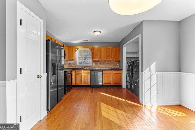 kitchen featuring a wainscoted wall, stainless steel dishwasher, brown cabinetry, washer and dryer, and a sink