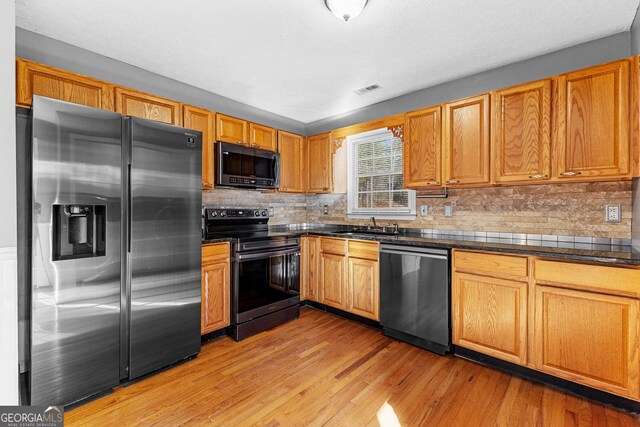 kitchen with visible vents, light wood-style flooring, a sink, appliances with stainless steel finishes, and dark countertops