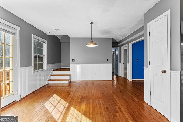 unfurnished dining area with a wainscoted wall, wood-type flooring, visible vents, and stairway