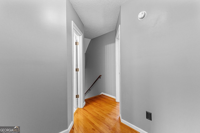 hallway with an upstairs landing, light wood-style flooring, a textured ceiling, and baseboards