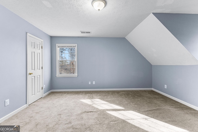 additional living space featuring baseboards, visible vents, vaulted ceiling, a textured ceiling, and carpet flooring