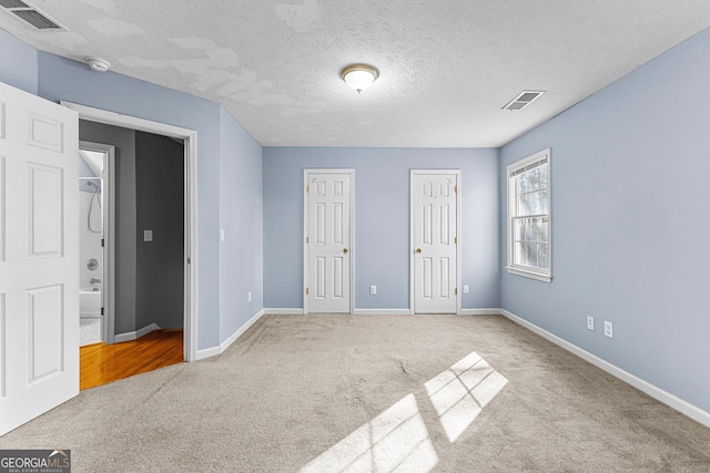 unfurnished bedroom featuring visible vents, multiple closets, a textured ceiling, carpet, and baseboards