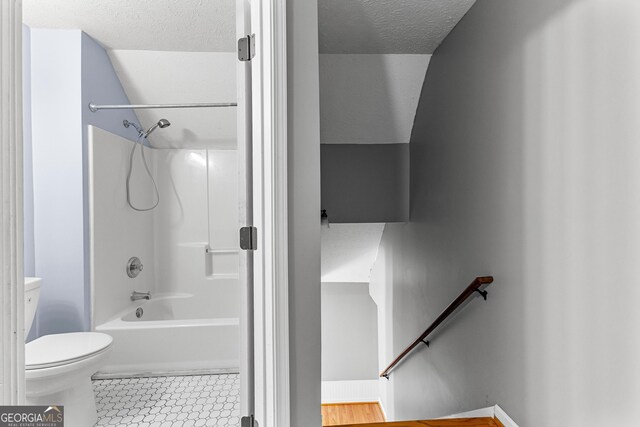 bathroom with tile patterned floors, toilet, washtub / shower combination, and a textured ceiling