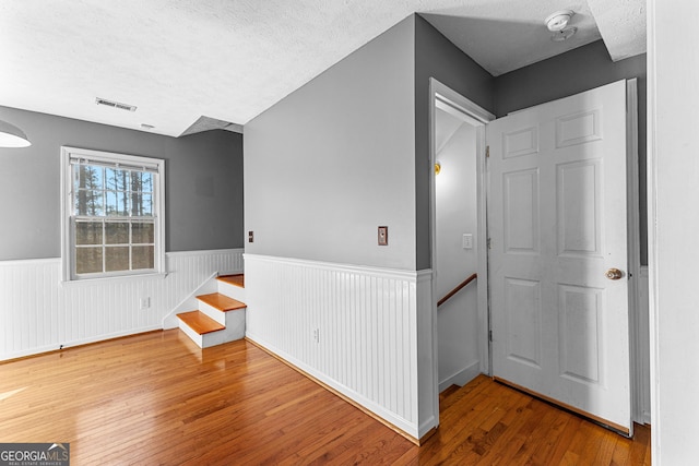 interior space with a textured ceiling, visible vents, wood-type flooring, and wainscoting