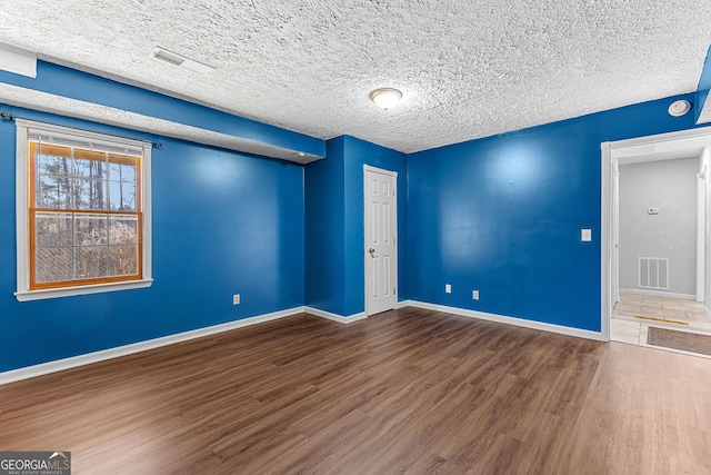 spare room with visible vents, a textured ceiling, baseboards, and wood finished floors