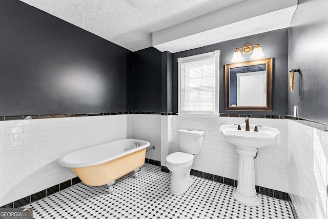 bathroom with a soaking tub, toilet, wainscoting, and a textured ceiling