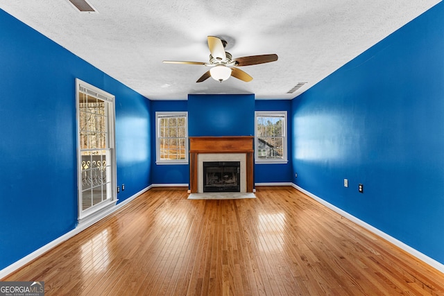 unfurnished living room featuring a ceiling fan, visible vents, baseboards, a fireplace with flush hearth, and wood-type flooring