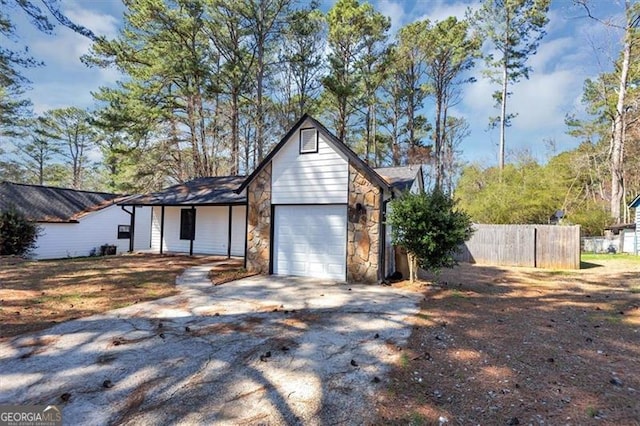 view of front facade featuring a garage, fence, stone siding, and driveway