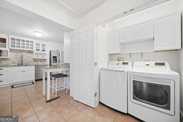 laundry area featuring washing machine and clothes dryer, cabinet space, light tile patterned flooring, and a sink