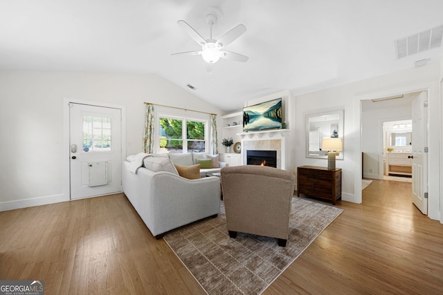 living area featuring visible vents, lofted ceiling, a lit fireplace, and wood finished floors