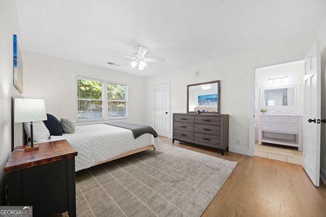 bedroom featuring visible vents, baseboards, wood finished floors, ensuite bath, and a ceiling fan