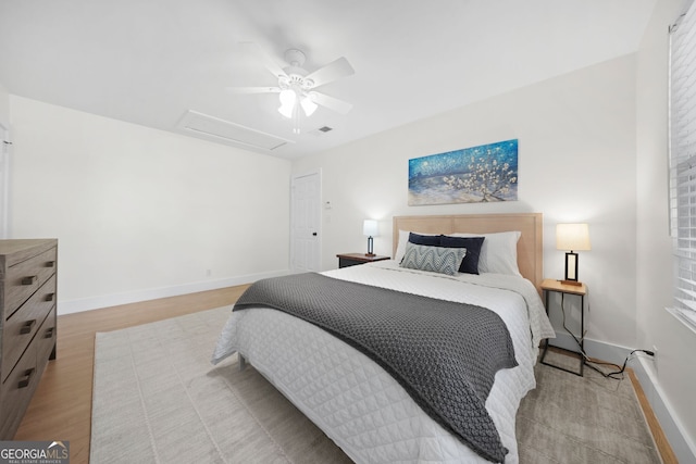 bedroom with visible vents, light wood-style floors, baseboards, attic access, and ceiling fan