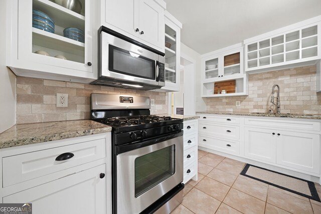 kitchen featuring a sink, appliances with stainless steel finishes, white cabinets, light tile patterned floors, and light stone countertops