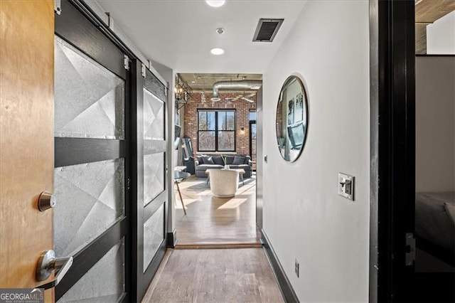 corridor with visible vents, wood finished floors, baseboards, and brick wall