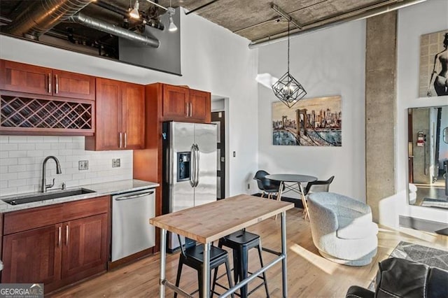 kitchen with decorative light fixtures, light wood-type flooring, a high ceiling, stainless steel appliances, and a sink