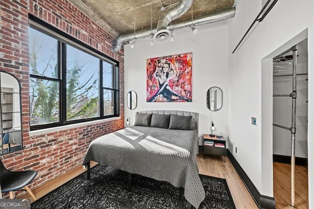 bedroom featuring visible vents, wood finished floors, brick wall, rail lighting, and baseboards