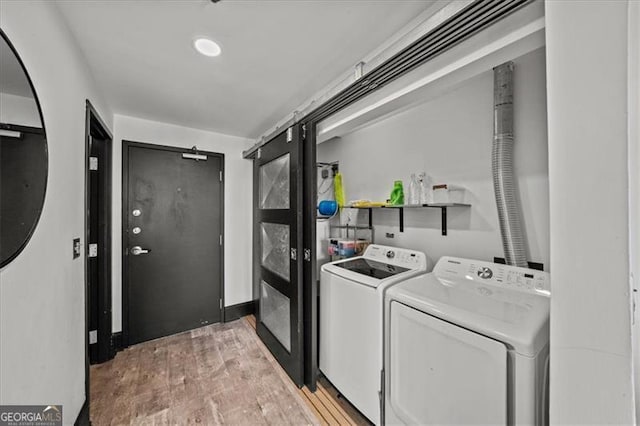 clothes washing area with laundry area, light wood-type flooring, a barn door, and separate washer and dryer