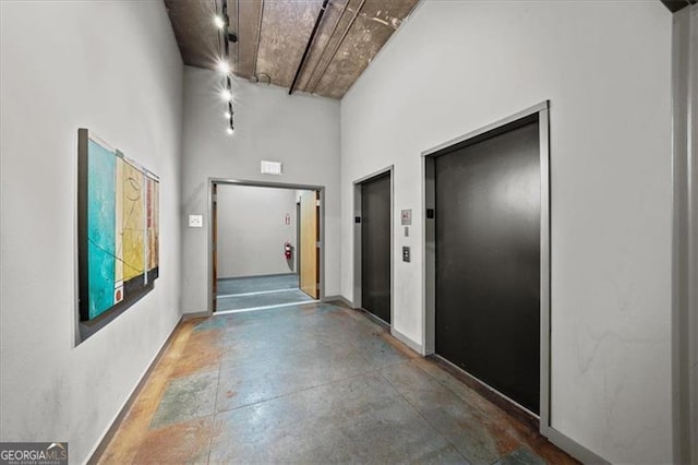 corridor featuring elevator, concrete floors, and a high ceiling