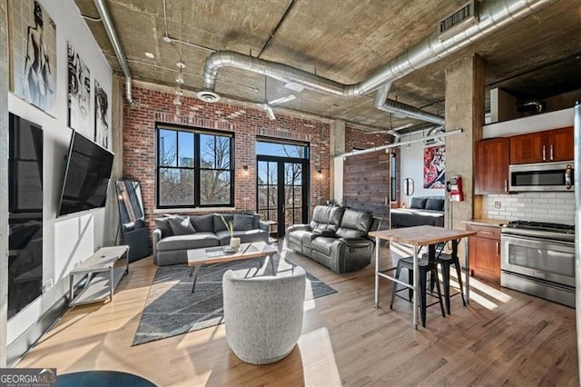 living room with a high ceiling, visible vents, light wood-type flooring, and brick wall