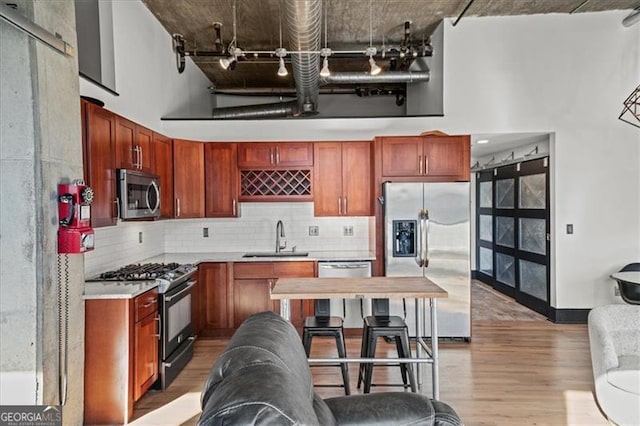 kitchen with backsplash, appliances with stainless steel finishes, a high ceiling, light wood-style floors, and a sink