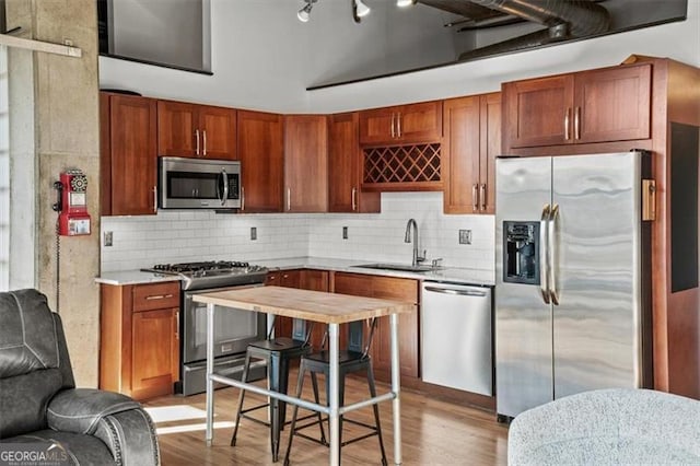 kitchen with light wood finished floors, a sink, stainless steel appliances, light countertops, and backsplash