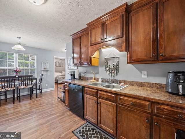 kitchen featuring light wood-style flooring, a sink, a textured ceiling, dishwasher, and hanging light fixtures