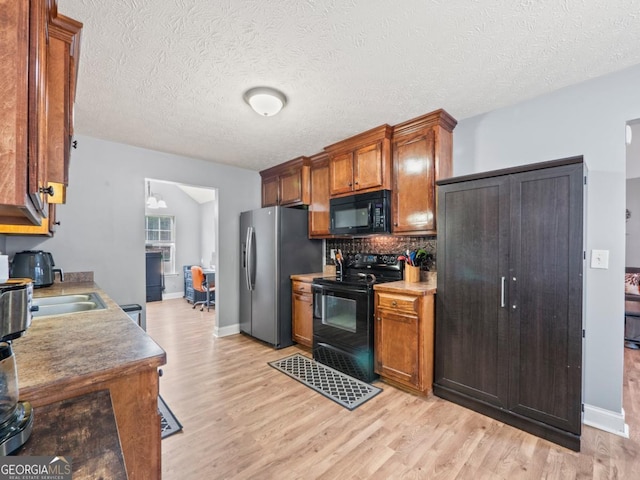 kitchen with brown cabinets, black appliances, light wood-style flooring, tasteful backsplash, and baseboards