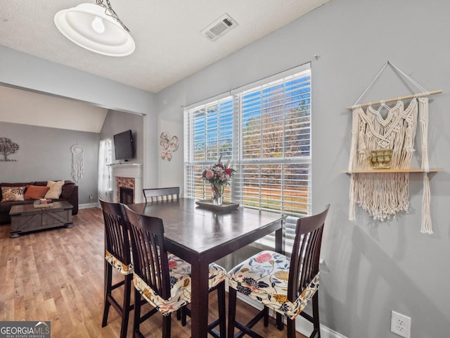 dining space with visible vents, baseboards, lofted ceiling, light wood-style flooring, and a fireplace