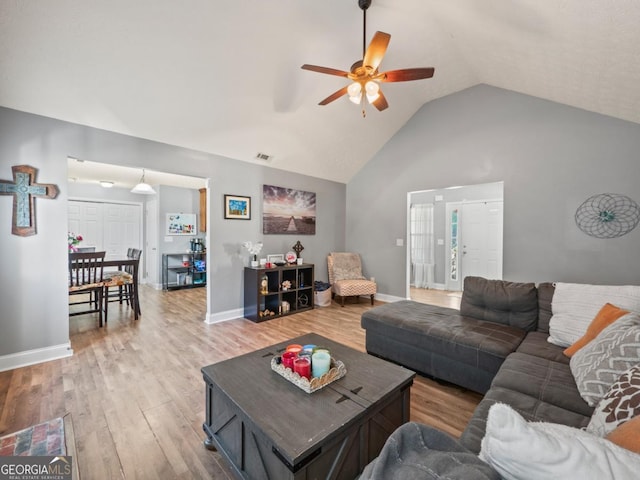 living area featuring baseboards, visible vents, high vaulted ceiling, ceiling fan, and light wood-style floors