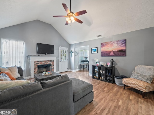 living room with visible vents, a brick fireplace, ceiling fan, vaulted ceiling, and wood finished floors