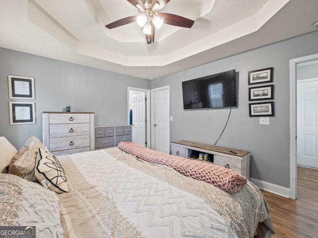 bedroom with ceiling fan, a raised ceiling, baseboards, and wood finished floors