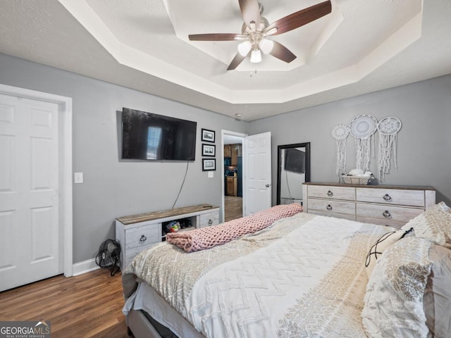 bedroom featuring ceiling fan, baseboards, a tray ceiling, and wood finished floors